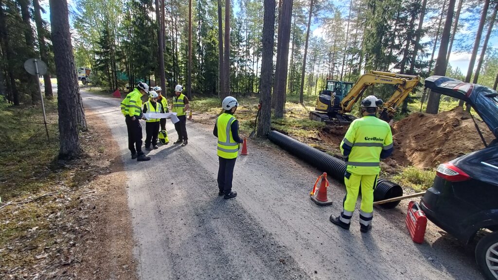 Rakennustyömaa, kaivinkone ja työmiehiä metsätiellä